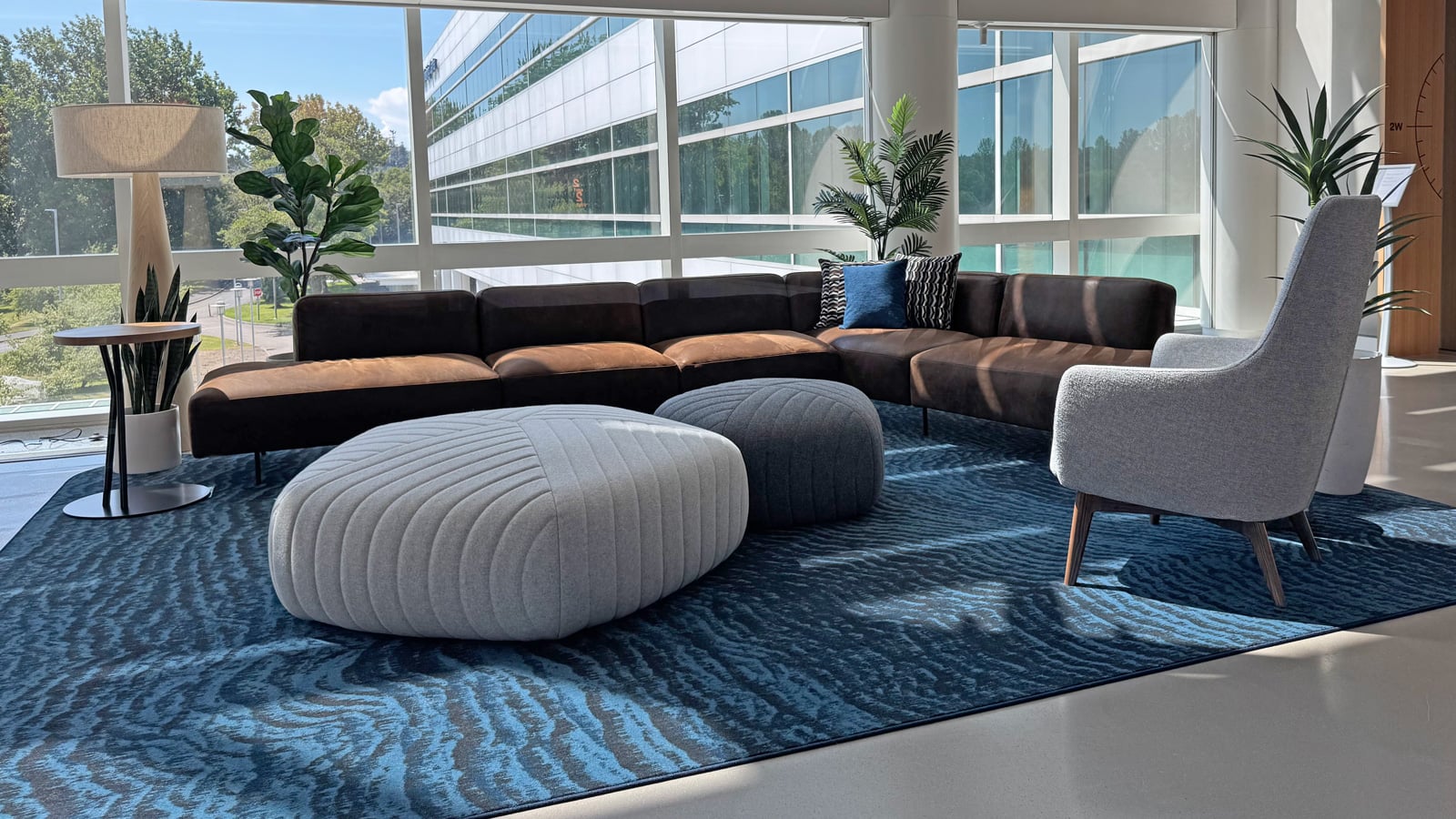 Office commons with leather sectional seating, upholstered poufs, and floor-to-ceiling windows