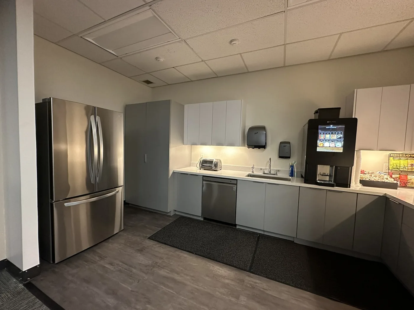 Refreshed office kitchenette from the doorway, with new cabinets, counters, and plank flooring